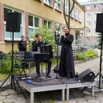 Kobieta ubrana w czarną suknię śpiewa podczas wydarzenia, obok mężczyzna grający na instrumencie 