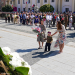 Młody chłopiec w mundurze składa kwiaty pod pomnikiem 