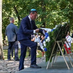Mężczyzna poprawia szarfę z wieńca kwiatowego znajdującego się pod pomnikiem  