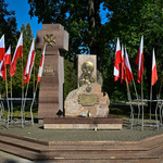 Pomnik Katyński, przy nim leżą znicze, wkoło stoją biało-czerwone flagi