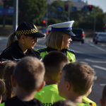 Na zdjęciu widać dzieci w kamizelkach odblaskowych wraz z funkcjonariuszami Policji i Straży Miejskiej