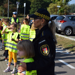 Na zdjęciu widać dzieci w kamizelkach odblaskowych wraz z funkcjonariuszami Policji i Straży Miejskiej