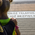 Na zdjęciu widać namalowany napis na chodniku, dzieci i strażnikami miejskiego