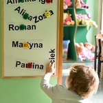 Dziecko podczas zabawy tablicą, na której znajdują się imiona dzieci