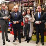 Uczestnicy konferencji prasowej trzymają w dłoni kubki świąteczne 