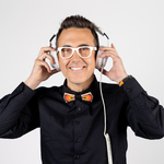 Dj Adamus pozuje do zdjęcia trzymając przy uszach białe słuchawki 