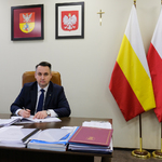 Zastępca prezydenta Przemysław Tuchliński siedzi za biurkiem, w dłoni trzyma pióro