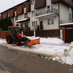Czerwony traktorek zgarnia śnieg z ulicy