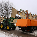 Zielony traktorek wrzuca śnieg do przyczepy