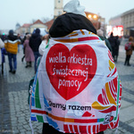 Kobieta owinięta flagą z czerwonym serduszkiem i napisem Wielka Orkiestra Świątecznej Pomocy