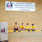 Czterech uczniów ubranych w żółte koszulki siedzi na podłodze 