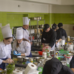 Uczestnicy konkursu kulinarnego podczas pracy na swoich stanowiskach. Juror obserwuje ich pracę.