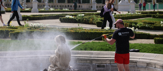 Mężczyzna myje pomnik znajdujący się w fontannie ogrodu Branickich, w tle spacerujący ludzie