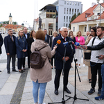 Dziennikarze trzymają mikrofony, do których przemawia Prezydent Miasta Białegostoku. W tle ratusz i sąsiadujące budynki