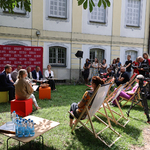 Urzędnicy oraz organizatorzy siedzą na pufach, obok stoją dziennikarze 