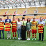 Uczestnicy konferencji stoją na murawie stadionu obok Pucharu Mistrza Polski