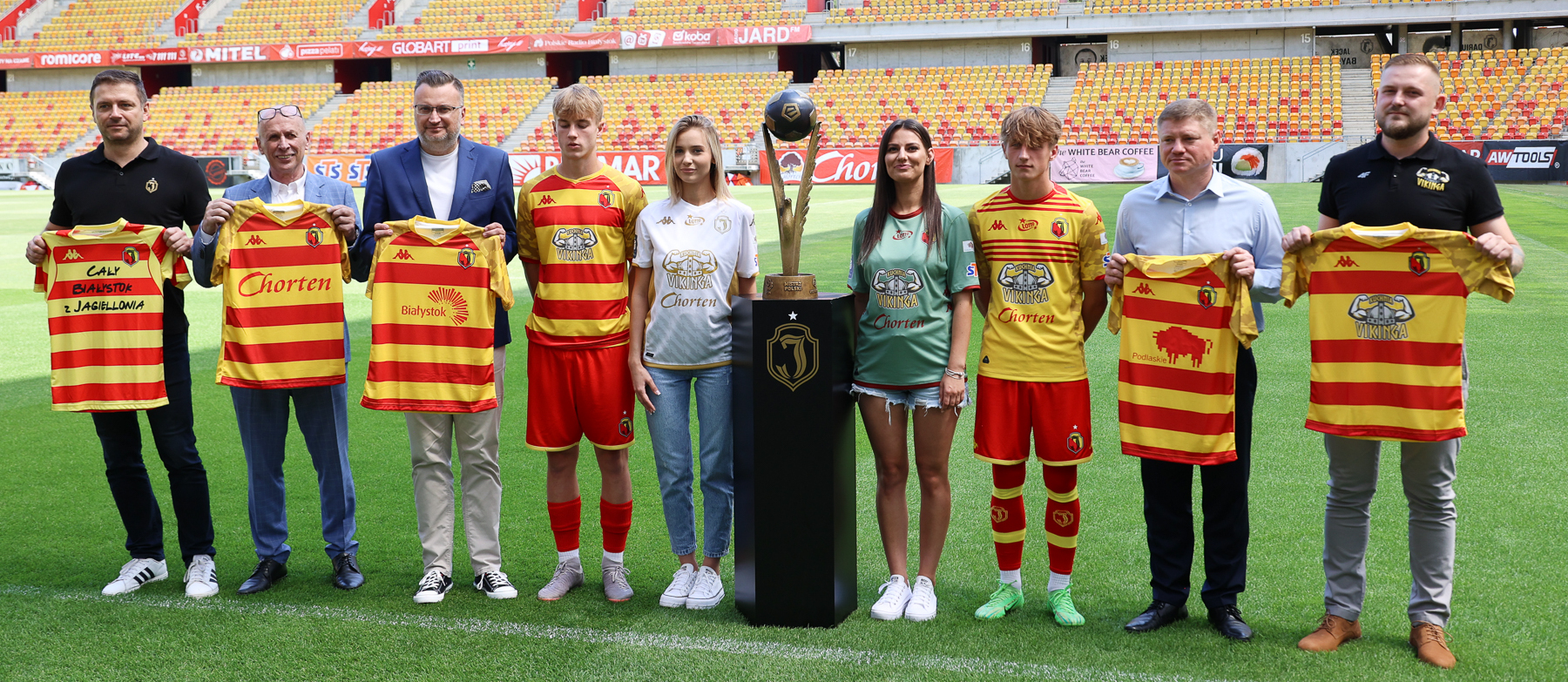 Uczestnicy konferencji stoją na murawie stadionu obok Pucharu Mistrza Polski