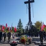 Pomnik w krztałcie krzyża, obok stoją mundurowi