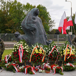 Mundurowi stoją z bronią obok pomnika pod którym leżą wieńce 