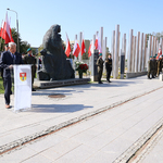 Prezydent Tadeusz Truskolaski przemawia do mikrofonu przy mównicy przy pomniku Matki Sybiraczki, w tle flagi Polski 