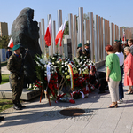 Kilka osób stoi przed pomnikiem Matki Sybiraczki, obok stoją mundurowi