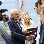 Prezydent Tadeusz Truskolaski podaje dłoń uczniowi, który stoi w szeregu obok innych uczniów, obok operator z kamerą nagrywa wydarzenie 