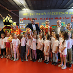 Dzieci w białych jednakowych koszulkach stoją razem z opiekunami obok zastępcy prezydenta Tomasza Klim oraz Agnieszki Krokos-Janczyło