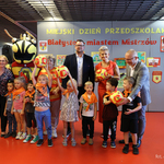 Dzieci z pomarańczowymi apaszkami na szyjach stoją na pierwszym planie, w tle stoi zastępca prezydenta Tomasz Klim oraz kurator podlaski Agnieszka Krokos-Janczyło
