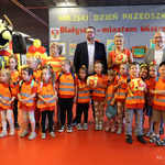 Przedszkolaki w pomarańczowych kamizelkach odblaskowych stoją wspólnie z opiekunem, zastępcą prezydenta Tomaszem Klim i kuratorem podlaskim Agnieszką Krokos-Janczyło podczas wydarzenia 