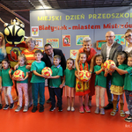 Dzieci w zielonych bluzkach trzymają piłki Jagiellonii, za nimi stoją zastępca prezydenta Tomasz Klim, kurator podlaski Agnieszka Krokos-Janczyło i opiekunowie  