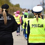 Uczniowie rozdają przechodniom odblaski, na pierwszym planie funkcjonariusze Straży Miejskiej i Policji
