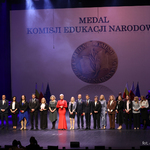 Nauczyciele wyróżnieni medalem stoją na scenie razem z kurator Agnieszka Krokos-Janczyło i wojewodą Jackiem Brzozowskim, w tle wyświetlona grafika 