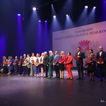 Prezydent Miasta Białegostoku stoi razem z grupą nauczycieli na scenie, w tle grafika z herbem miasta i tekstem 