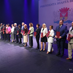 Nauczyciele stoją w rzędzie na scenie trzymając listy gratulacyjne w dłoniach, po środku stoi Prezydent Miasta Białegostoku