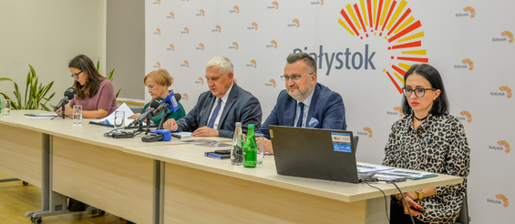 Prezydent Tadeusz Truskolaski, skarbnik Stanisława Kozłowska, rzecznik prasowy Urszula Buoblej i inni uczestnicy konferencji siedzą przy stole na którym stoją mikrofony