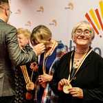 Kobieta uśmiecha się i trzyma medal zawieszony na szyi, w tle zastępca prezydenta Rafał Rudnicki nakłada medale kolejnym osobom.