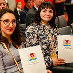 Dwie uczestniczki nagrodzone medalami siedzą i trzymają w rękach listy gratulacyjne od Prezydenta Miasta Białegostoku.