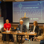 Uczestnicy konferencji siedzą przy stole, na którym stoja mikrofony.