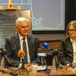 Prezydent Tadeusz Truskolaski mówi do mikrofonów stojących na stole podczas konferencji, obok siedzi kobieta.