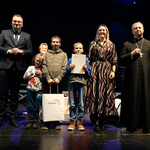 Zastępca prezydenta Rafał Rudnicki oraz duchowny stoją z kilkoma laureatami konkursu.