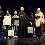 Kilkoro laureatów konkursy stoi na scenie trzymając białe torby z logo Białegostoku, obok stoją zastępca prezydenta Rafał Rudnicki i duchowny.