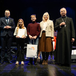 Laureaci konkursy z opiekunem stoją na scenie z zastępcą prezydenta Rafałem Rudnickim i duchownym.