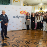 Uczennica recytuje wiersz, obok stoi prezydent Tadeusz Truskolaski, po prawej stronie stoją uczestnicy wydarzenia.