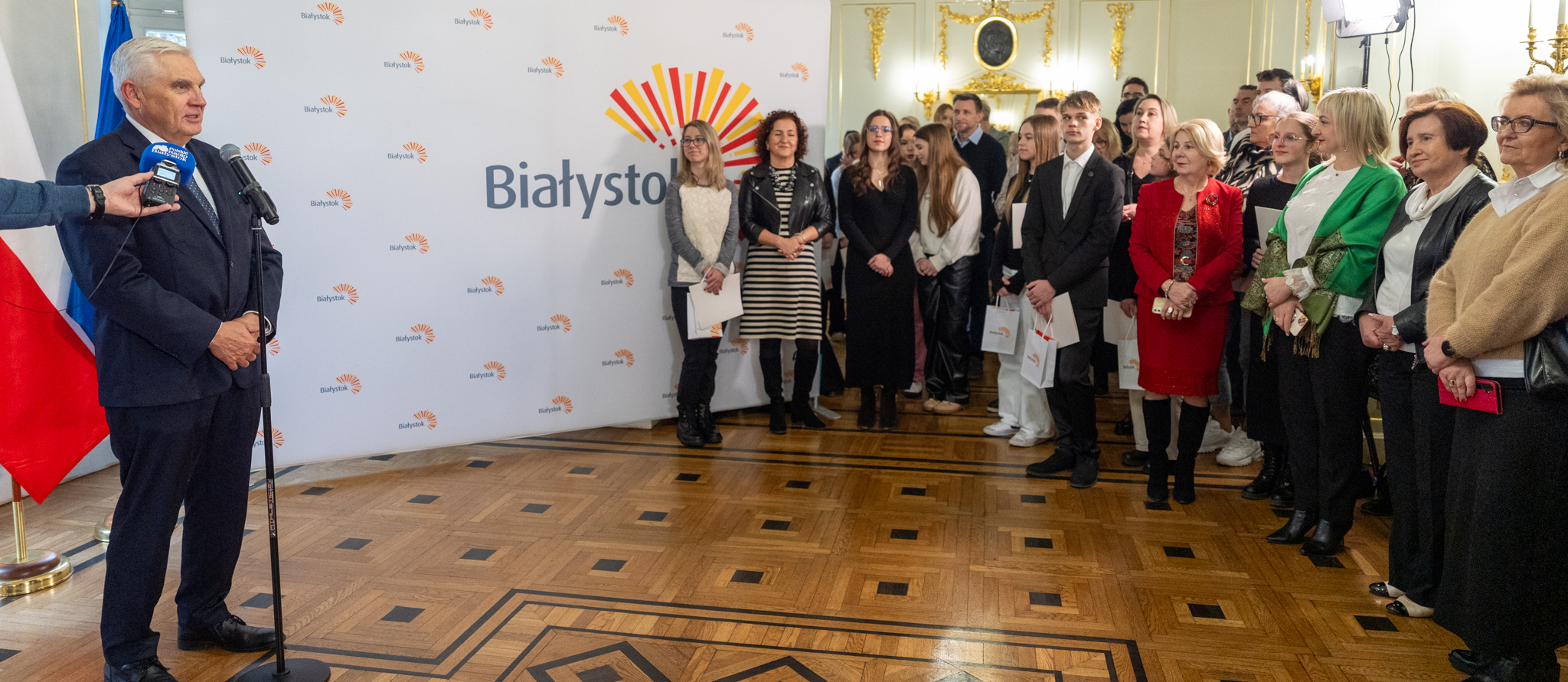 Uczennica recytuje wiersz, obok stoi prezydent Tadeusz Truskolaski, po prawej stronie stoją uczestnicy wydarzenia.