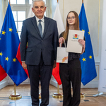 Uczennica trzyma list gratulacyjny i niewielką białą torebkę z logo miasta Białegostoku, obok stoi prezydent Tadeusz Truskolaski.