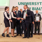 Dwie kobiety odbierają dyplom z rąk mężczyzny, obok stoją inni uczestnicy wydarzenia.