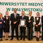 Siedem osób stoi obok siebie, mężczyzna trzyma dyplom.