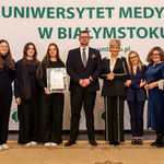 Siedem osób stoi, młoda kobieta trzyma dyplom.