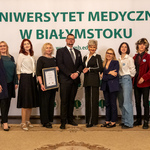 Dziesięć osób stoi, kobieta trzyma dyplom.