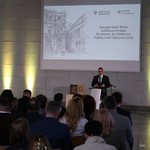 Zastępca prezydenta Tomasz Klim przemawia do mikrofonu, na pierwszym planie siedzą uczestnicy wydarzenia, w tle wyświetlany jest tekst „Inauguracja Roku Jubileuszowego Wydziału Architektury Politechniki Białostockiej”.